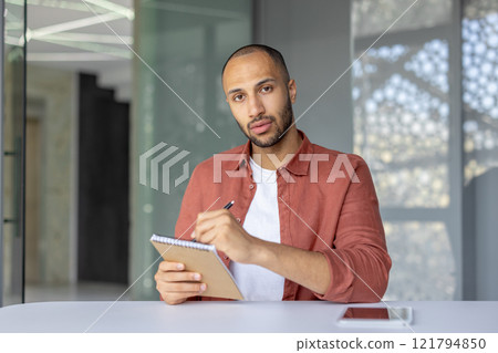 Webcam view, serious focused man looking into camera listening to online business meeting and remote conference with colleagues, businessman working in the middle of office at workplace. 121794850