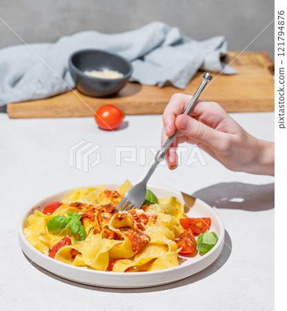 Hand holding fork with tagliatelle or pappardelle pasta with tomato sauce, basil and parmesan cheese Hand holding fork with tagliatelle or pappardelle pasta with tomato sauce, basil and parmesan cheese 121794876