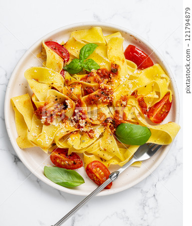 Tagliatelle or pappardelle pasta with tomato sauce, basil and parmesan cheese in a plate with fork Tagliatelle or pappardelle pasta with tomato sauce, basil and parmesan cheese in a plate with fork 121794879