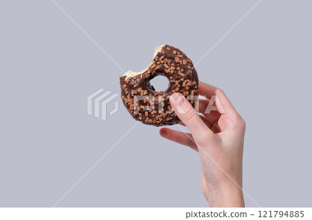 Hand holding glazed chocolate bite donut on blue background. 121794885