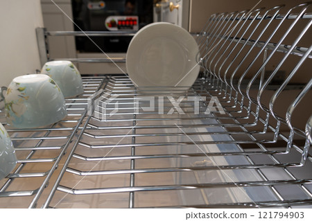 A clean and organized kitchen setup featuring a chrome dish rack with plates and cups. 121794903