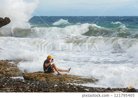 a man takes a dangerous selfie near the raging waves of the ocean a man takes a dangerous selfie near the raging waves of the ocean 121795405