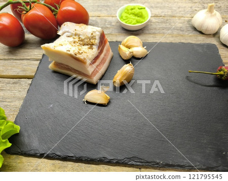 Juicy piece of lard on a sliced, granite board surrounded by vegetables an.. 121795545