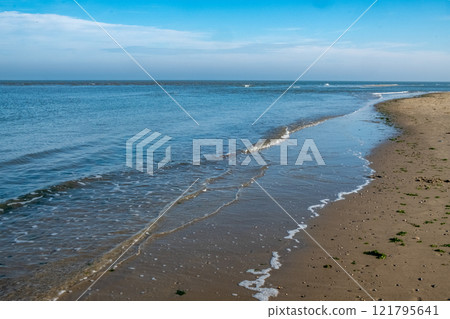 A serene and tranquil beachscape features gently rolling waves under expansive blue skies A serene and tranquil beachscape features gently rolling waves under expansive blue skies 121795641