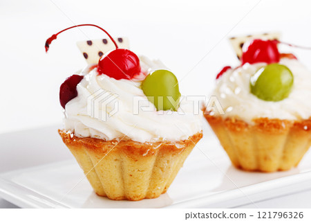 Beautiful cream cakes with cherries and grapes on a plate on a white background Beautiful cream cakes with cherries and grapes on a plate on a white background 121796326
