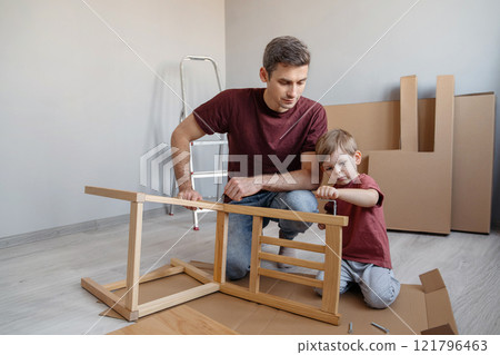 A father and his young son assemble wooden furniture at home 121796463