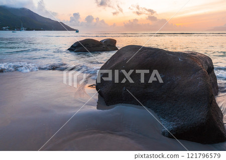 Coastal landscape with wet sand and silhouettes of rocks at sunset 121796579