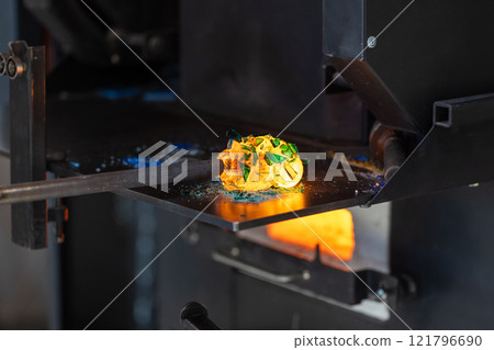 Molten glass fusing with colorful fragments on a blowing pipe Molten glass fusing with colorful fragments on a blowing pipe 121796690