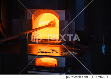 Molten glass on a blowpipe inside of open furnace, glass blowing Molten glass on a blowpipe inside of open furnace, glass blowing 121796691