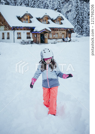 little girl walking on a snow in front of wooden house little girl walking on a snow in front of wooden house 121798206