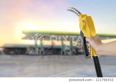 Holding a fuel nozzle against with gas station blurred background 121798358