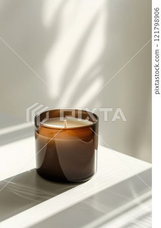 This elegant white aroma wax candle in a brown glass container is gracefully displayed on a minimalistic surface, illuminated by soft natural light 121798906