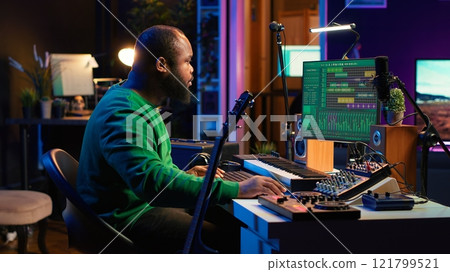 Musical producer prepares to record tunes on acoustic instrument, working in personal home studio to record soundtrack. Sound composer recording guitar music, editing with mixing console. Camera A. Musical producer prepares to record tunes on acoustic instrument, working in personal home studio to record soundtrack. Sound composer recording guitar music, editing with mixing console. Camera A. 121799521