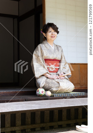 A woman in a kimono sitting in seiza on the veranda 121799569