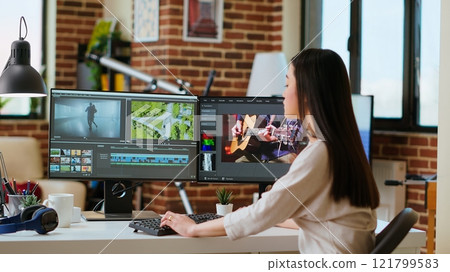 Female filmmaker working on post production from home office, editing timelines and color grading for a video shoot. Tech driven workspace showcases a digital workflow for video production. Camera B. Female filmmaker working on post production from home office, editing timelines and color grading for a video shoot. Tech driven workspace showcases a digital workflow for video production. Camera B. 121799583