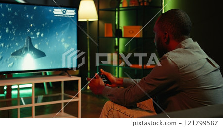 Gamer using controller and headphones to play first person shooter videogame on large smart TV. Man in home theatre using high tech gaming console gamepad to defeat foes, camera B Gamer using controller and headphones to play first person shooter videogame on large smart TV. Man in home theatre using high tech gaming console gamepad to defeat foes, camera B 121799587