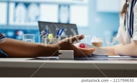 Woman specialist taking pulse and blood pressure for african american patient, consulting a man during check up visit. Doctor doing a cardiac control measurements, blood pressure monitor. Camera A. 121799630