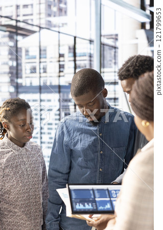 African american staff gathers and examines monthly revenue balance on a tablet, planning next steps in financial operations. Workers reviewing performance data and setting company objectives. African american staff gathers and examines monthly revenue balance on a tablet, planning next steps in financial operations. Workers reviewing performance data and setting company objectives. 121799653