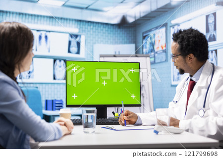 African american medic points at green screen on computer while he consults his patient, exploring treatment plans on health insurance. Physician gives medical advice to ill woman. 121799698