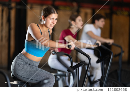 Focused girl works out with airbike during class at fitness club Focused girl works out with airbike during class at fitness club 121802668
