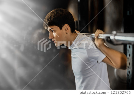 Slender guy trains muscles of arms and back using barbell and differentiated weighting in gym Slender guy trains muscles of arms and back using barbell and differentiated weighting in gym 121802765