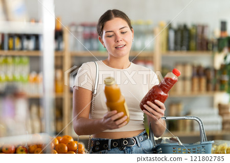Young woman buyer chooses tomato and peach juices Young woman buyer chooses tomato and peach juices 121802785