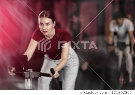Focused girl works out with exercise bicycle during class at fitness club Focused girl works out with exercise bicycle during class at fitness club 121802803