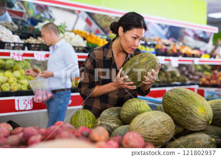 Female shopper choosing ripe melon on counter at farmers market Female shopper choosing ripe melon on counter at farmers market 121802937