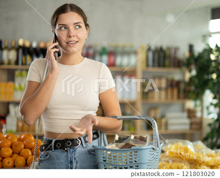 Young woman choosing groceries while talking on phone Young woman choosing groceries while talking on phone 121803020