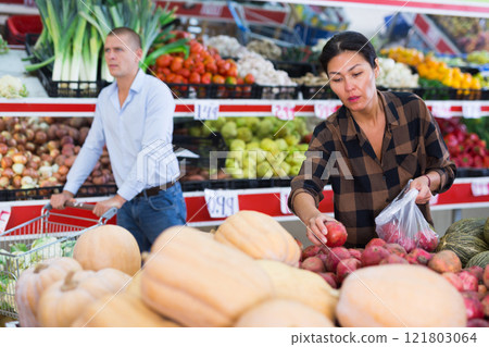 Asian woman choosing pomegranates on counter in greengrocery Asian woman choosing pomegranates on counter in greengrocery 121803064