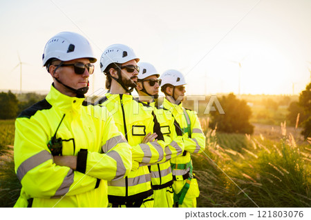 Group portrait of electrical engineers team pose to camera against the sunset nature in background. Engineers in fully safety suit and headwear are posing to camera. Group portrait of electrical engineers team pose to camera against the sunset nature in background. Engineers in fully safety suit and headwear are posing to camera. 121803076