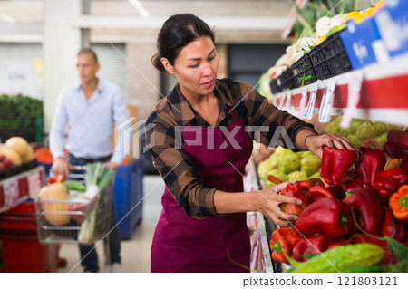 Woman in apron stacking red peppers in greengrocer 121803121