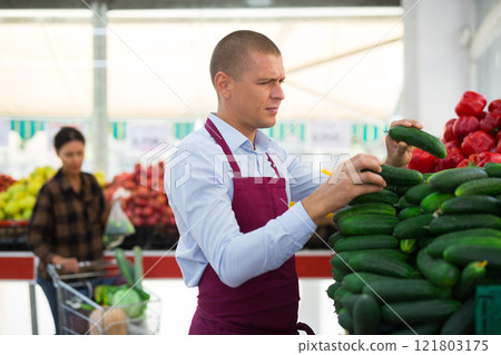 Greengrocer worker stacking cucumbers 121803175