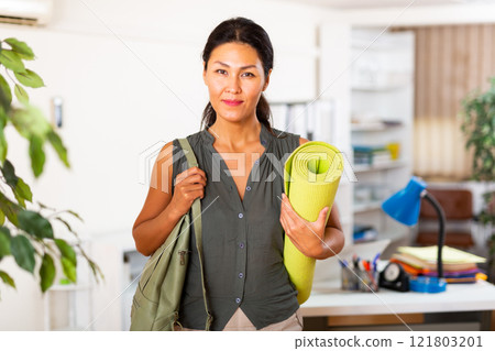 Asian businesswoman holding yoga mat in office 121803201