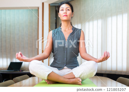 Businesswoman sitting at the table in lotus position Businesswoman sitting at the table in lotus position 121803207