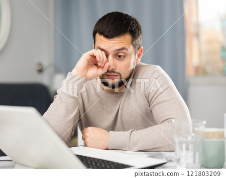 Man rubs tired eyes with his hands after a long work at laptop at home Man rubs tired eyes with his hands after a long work at laptop at home 121803209