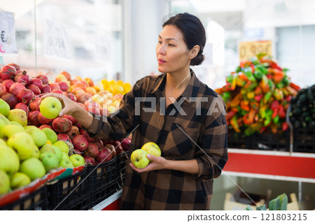 Woman choosing apples in greengrocer Woman choosing apples in greengrocer 121803215