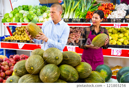 Saleswoman helping male buyer to choose melon in store Saleswoman helping male buyer to choose melon in store 121803256