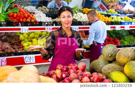 Friendly saleswoman offering fruits and vegetables in greengrocery store 121803259