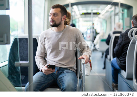 Young man with suitcase and phone traveling in streetcar 121803378
