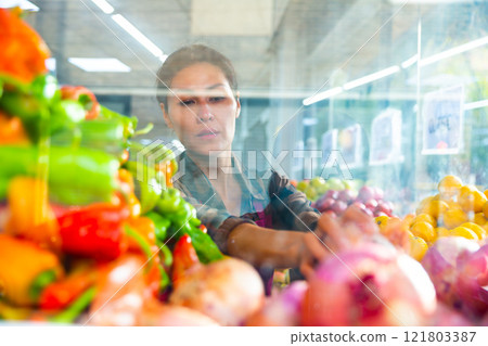 Asian saleswoman working behind glass showcase of greengrocery Asian saleswoman working behind glass showcase of greengrocery 121803387
