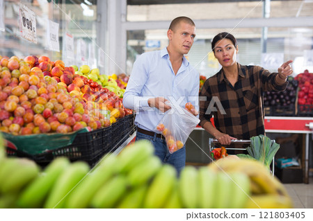 Family couple looking for fruits and vegetables in greengrocery Family couple looking for fruits and vegetables in greengrocery 121803405