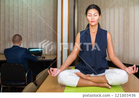 Businesswoman sitting at the table in lotus position 121803436