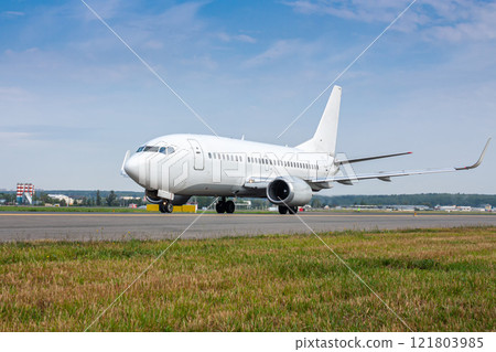 White passenger airliner taxiing on the main taxiway White passenger airliner taxiing on the main taxiway 121803985