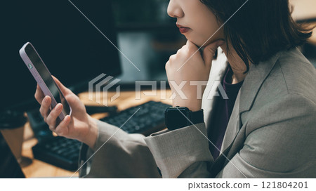 Woman/businesswoman thinking while looking at her smartphone 121804201