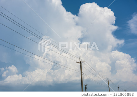 View of utility poles with blue sky and white clouds as a background. 121805898