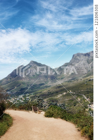 Sandy path through a landscape with mountains against a cloudy blue sky background with copy space. Peaceful and scenic view of a rugged hiking trail to explore on a walk while in nature outdoors 121806308