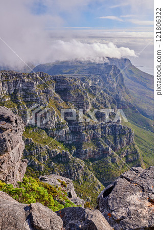 Beautiful landscape of rocky mountains with a cloudy blue sky on a summer day. Peaceful and scenic view of a peak with large rocks and grass. A summit in nature covered by clouds 121806322