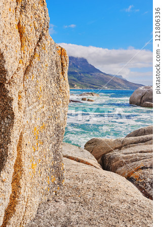 Stunning seaside location for a summer holiday in Cape Town. Boulders at a beach with ocean waves and water washing over rocks at the coast with mountain and blue sky with clouds in the background Stunning seaside location for a summer holiday in Cape Town. Boulders at a beach with ocean waves and water washing over rocks at the coast with mountain and blue sky with clouds in the background 121806336