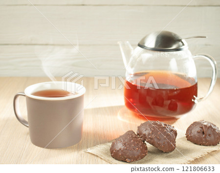 Morning breakfast. Glass teapot with tea, mug and chocolate marshmallows in the foreground 121806633